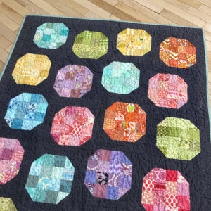 May include: A quilt with a dark gray background and 16 octagonal patches of various colorful fabrics. Each patch is made of smaller squares of different patterns and colors.