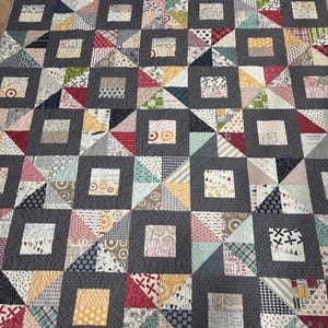 May include: A handmade quilt with a patchwork design. The quilt features a repeating pattern of gray squares framing smaller squares and triangles in various colors and patterns, including red, blue, and yellow. The quilt is made of fabric.