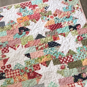 May include: A white quilt with a patchwork design featuring a variety of colorful fabrics. The quilt is made up of small squares and rectangles in shades of red, green, blue, and pink. The quilt is quilted with a simple stitch pattern.