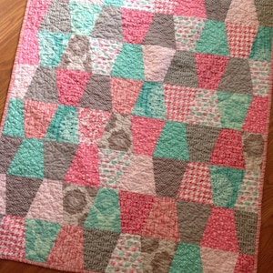 May include: A patchwork quilt with a geometric pattern in shades of pink, teal, and gray. The quilt is made of various fabrics with different patterns, including floral, polka dot, and plaid.