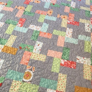 May include: A gray quilt with a patchwork design featuring various shades of green, orange, and pink. The quilt is made of fabric with floral and geometric patterns.