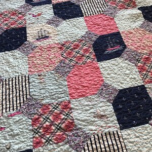 May include: A patchwork quilt with a nautical theme. The quilt is made of various fabrics, including pink, blue, white, and plaid. The quilt features anchors, ships, and stripes.