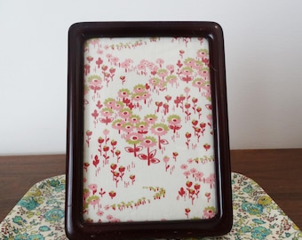 May include: A rectangular picture frame with a dark brown, smooth, rounded border. The frame contains a white insert featuring a repeating pattern of small pink and light green stylized flowers with thin stems on a cream-colored background.