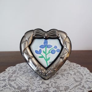 Puede incluir: Una taza de cerámica blanca con un asa negra y el texto "But First, Coffee" en negrita negra. La taza se encuentra sobre un fondo neutro, resaltando su diseño simple.