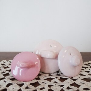 May include: Three ceramic lids in various shades of pink. The lids are round and have a small knob on top. The lids are sitting on a white crocheted doily.