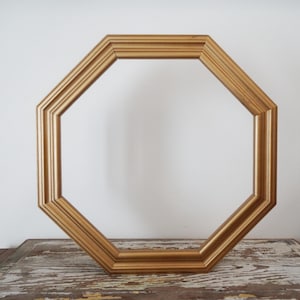 May include: An octagonal picture frame with a metallic gold finish. The frame features a multi-tiered, stepped profile with clean, straight edges and mitered corners, creating a geometric shape that is hollow in the centre.