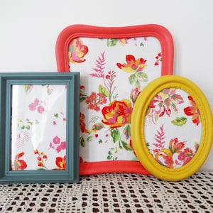 Peut inclure: Trois cadres photo avec du papier à motifs floraux à l'intérieur. Les cadres sont peints dans différentes couleurs : corail, sarcelle et jaune.
