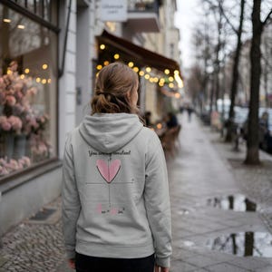 Puede incluir: Una sudadera con capucha gris claro con un gráfico en la espalda. El gráfico incluye un corazón rosa, un gráfico matemático y el texto "You are my constant" y "Love = im²". La sudadera tiene capucha y cordón.