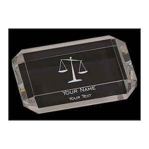 May include: A rectangular crystal award with a black interior. The award features a white scale of justice symbol and the text "YOUR NAME" and "YOUR TEXT". The edges of the award are faceted.