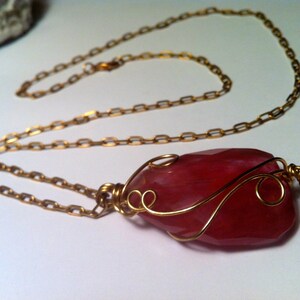 May include: A pink gemstone pendant necklace with a gold chain and wire wrapping. The gemstone is a unique shape and has a natural, organic look.