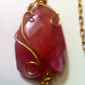 May include: A pink gemstone pendant with gold wire wrapping. The pendant is attached to a gold chain.