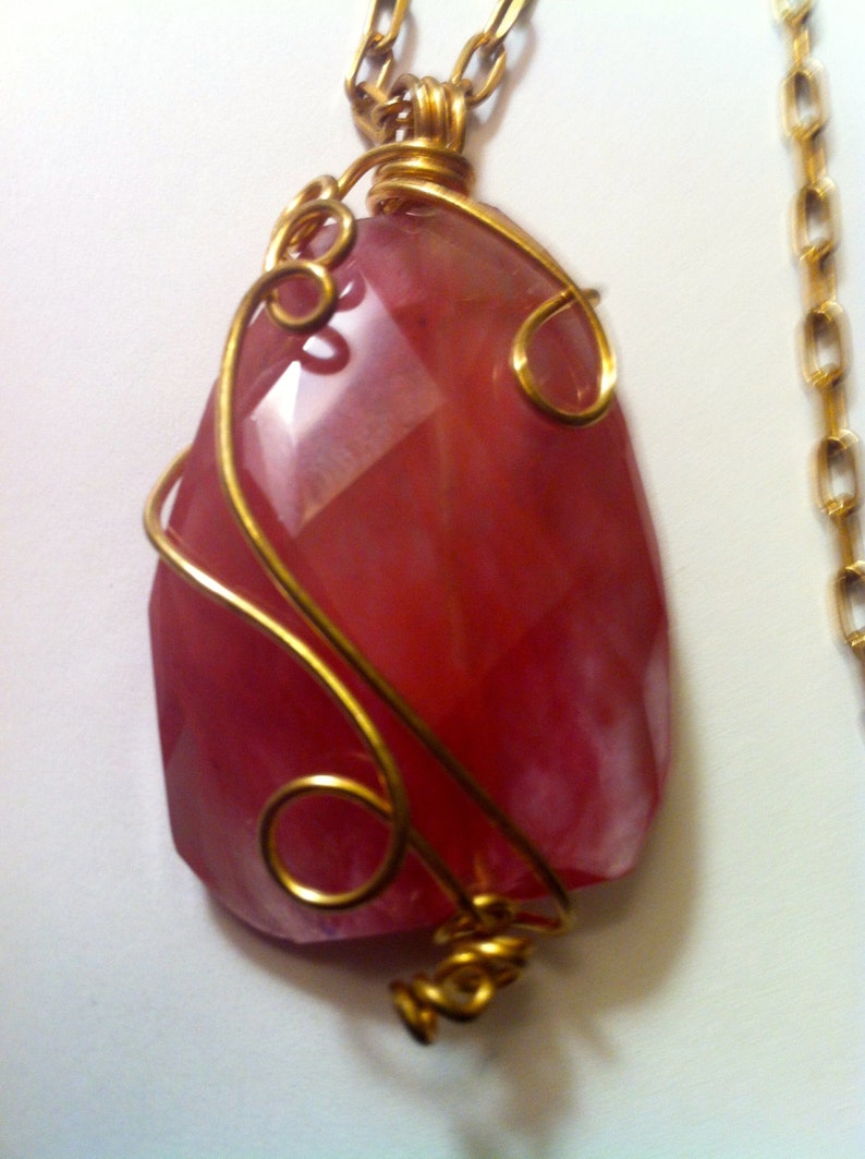 May include: A pink gemstone pendant with gold wire wrapping. The pendant is attached to a gold chain.