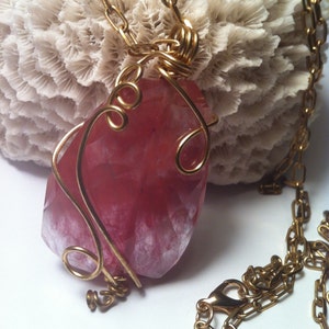 May include: A gold chain necklace with a pink and white gemstone pendant wrapped in gold wire.