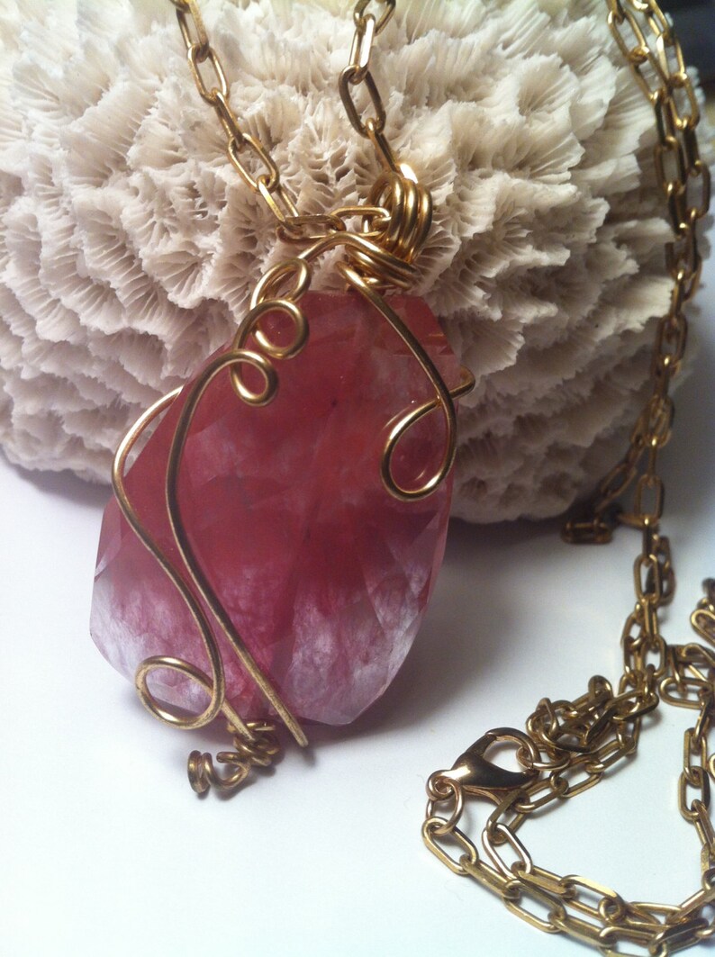 May include: A gold chain necklace with a pink and white gemstone pendant wrapped in gold wire.