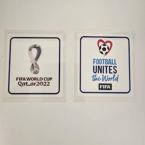 Può includere: Due adesivi quadrati con sfondi bianchi e bordi blu. Uno presenta il logo della Coppa del Mondo FIFA Qatar 2022. L'altro ha un pallone da calcio all'interno di un cuore, con la scritta "FOOTBALL UNITES the World" e il logo FIFA.