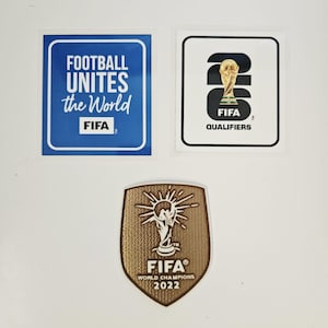Pode incluir: Três adesivos e patches com tema da FIFA. Um adesivo quadrado azul com o texto branco "FOOTBALL UNITES the World" e o logotipo da FIFA. Um adesivo branco apresenta o troféu da FIFA e "QUALIFIERS". Um patch dourado exibe o troféu da FIFA e "WORLD CHAMPIONS 2022".
