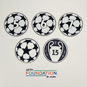 Könnte beinhalten: Eine Sammlung von Fußball-Patches in Schwarz und Weiß, mit den Zahlen 5, 6 und 7, sowie ein Patch mit der Zahl 15 in einer Trophäe. Ebenfalls enthalten ist ein rechteckiger Patch mit dem Text "UEFA FOUNDATION for children".