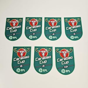 Op de afbeelding: Zeven groene en witte Carabao Cup-patches met de nummers 2, 3, 4, 5, 6, 8 en 10. Elke patch heeft een logo van een stierschedel, de tekst "Carabao Cup" en "EFL".