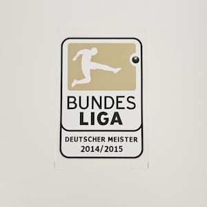 Könnte beinhalten: Ein Aufkleber mit dem Bundesliga-Logo. Das Logo zeigt eine weiße Silhouette eines Fußballspielers auf beigem Hintergrund. Die Worte "BUNDES LIGA" und "DEUTSCHER MEISTER 2014/2015" sind in Schwarz gedruckt, mit schwarzem Rand.