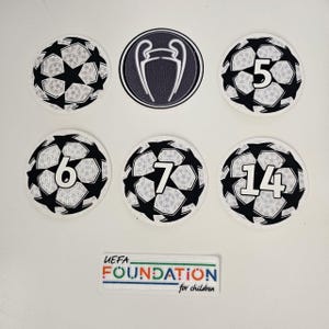 Può includere: Una collezione di toppe a tema calcio. Le toppe includono disegni di palloni da calcio, i numeri 5, 6, 7 e 14 e un logo della UEFA Champions League. È inclusa anche una toppa rettangolare con la scritta "UEFA FOUNDATION for children".