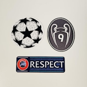 Può includere: Tre toppe ricamate: un pallone da calcio con stelle nere, un ovale bianco e nero con un trofeo e il numero 9 e un rettangolo blu con la scritta "RESPECT" e un logo UEFA.