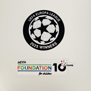 May include: Two stickers. The top sticker is a black circle with the text "UEFA EUROPA LEAGUE" and "2025 WINNERS" around a soccer ball graphic. The bottom sticker reads "UEFA FOUNDATION for children" with "10 YEARS" text.