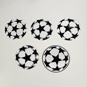 Può includere: Cinque adesivi circolari con un design a pallone da calcio in bianco e nero. Ogni adesivo ha uno sfondo bianco con un motivo a stelle nere. Gli adesivi sono disposti su una superficie bianca.