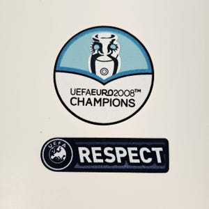 Puede incluir: Dos parches con texto y logotipos. El parche superior es un diseño circular con un fondo azul claro y el texto "UEFA EURO 2008 CHAMPIONS". El parche inferior tiene la palabra "RESPECT" y un logotipo de la UEFA.