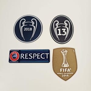 Può includere: Quattro toppe con loghi relativi al calcio. Due toppe circolari con un design a trofeo e gli anni 2018 e 13. Una toppa rettangolare con la parola "RESPECT" e un logo UEFA. Una toppa dorata a forma di scudo con un trofeo FIFA e "WORLD CHAMPIONS 2018".