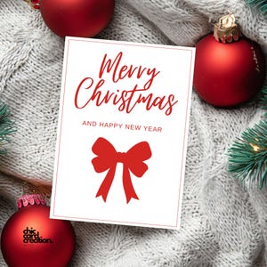 Könnte beinhalten: Eine weiße Weihnachtskarte mit rotem Text "Merry Christmas AND HAPPY NEW YEAR" und einer roten Schleifenillustration. Die Karte ist von roten Kugeln und grünen Tannenzweigen auf grauem Strickhintergrund umgeben.