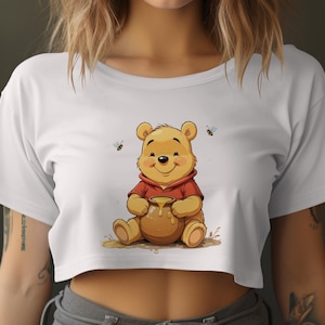 Op de afbeelding: Wit gecropped T-shirt met een cartoon afbeelding van Winnie de Poeh die een pot honing vasthoudt. Er zijn kleine bijen afbeeldingen rond Winnie de Poeh.