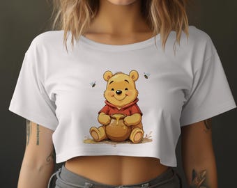 May include: White cropped t-shirt with a cartoon image of Winnie the Pooh holding a pot of honey.  There are small bee images around Winnie the Pooh.