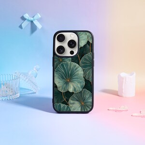 Può includere: Custodia per telefono nera con un motivo a foglie verdi e dorate. La custodia ha un bordo nero e un ritaglio per la fotocamera. Il design include grandi foglie stilizzate con venature dorate. Lo sfondo è una sfumatura di blu, rosa e giallo.