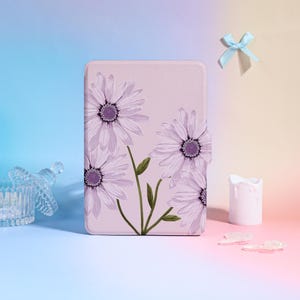 May include: A rectangular, light pink case featuring a floral design of lavender daisies with green stems and leaves. The daisies have a dark purple center. The background gradient transitions from blue to pink.