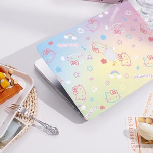 May include: A laptop computer with a colorful Hello Kitty design on the case. The design features a rainbow gradient background with Hello Kitty characters, stars, rainbows, and musical notes.