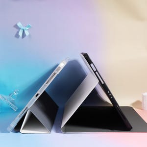 Pode incluir: Duas capas para tablets, uma transparente e outra preta, s&atilde;o exibidas. A capa transparente tem uma moldura transparente com uma fileira de pequenos orif&iacute;cios. A capa preta tem um design minimalista. Ambas as capas est&atilde;o anguladas, mostrando o interior.