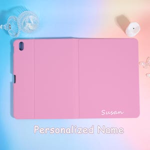 Pode incluir: Uma capa de tablet rosa com o nome "Susan" em escrita branca. A capa est&aacute; fechada e tem uma superf&iacute;cie lisa. As palavras "Personalized Name" est&atilde;o na parte inferior da imagem.