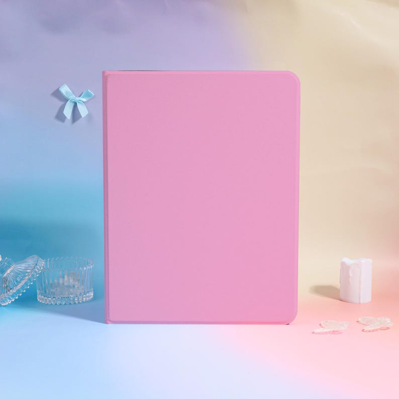Pode incluir: Uma capa de tablet rosa liso est&aacute; em p&eacute; contra um fundo gradiente de azul, roxo e amarelo. Uma pequena fita azul est&aacute; presa ao fundo. Tigelas de vidro decorativas e uma vela branca est&atilde;o em primeiro plano.