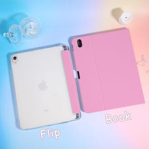 Pode incluir: Uma capa de tablet rosa com um suporte para caneta correspondente e um tablet branco. A capa est&aacute; aberta, revelando a tela do tablet. A palavra "Flip" est&aacute; escrita na parte inferior esquerda e "Book" na inferior direita.