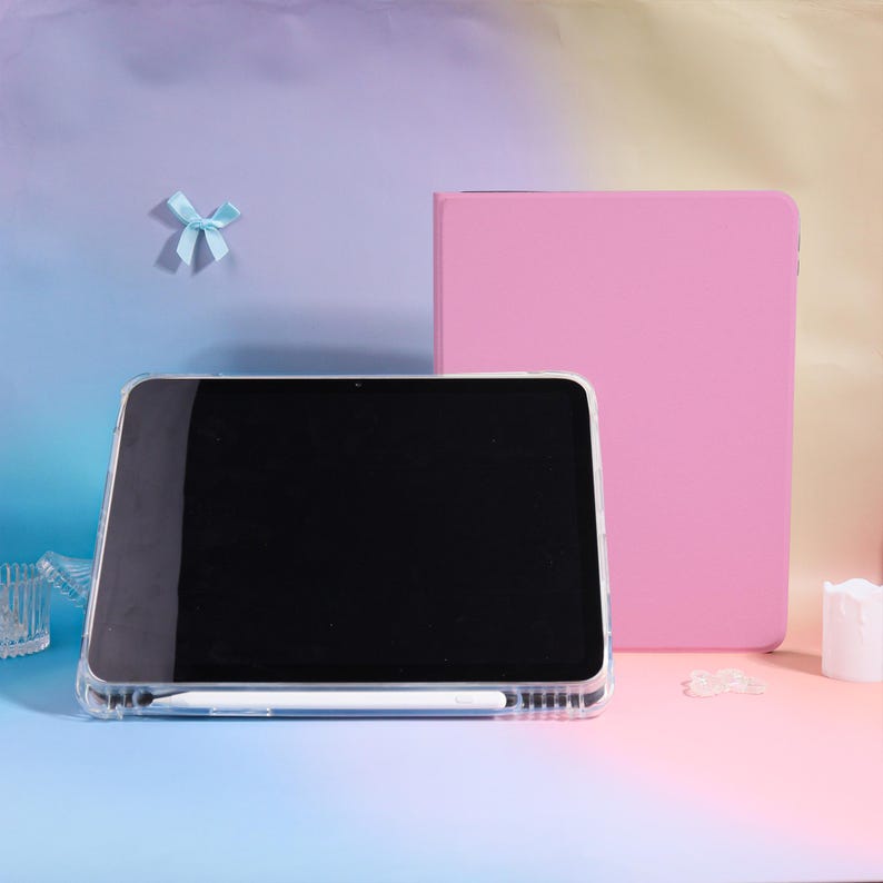 Pode incluir: Uma capa de tablet transparente com uma caneta branca e uma capa de tablet rosa. A tela do tablet &eacute; preta. Uma pequena fita azul est&aacute; no fundo. O fundo &eacute; um gradiente de azul, rosa e amarelo.