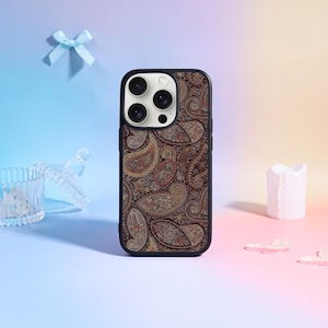 May include: A black phone case with a paisley pattern in shades of brown, gold, and blue. The case has a black border and a camera cutout. The phone case is a protective accessory for a smartphone.