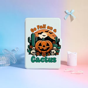 May include: A white rectangular case featuring a Halloween-themed design. The design includes a jack-o'-lantern, cacti, skulls, and the text "Go Fall on a Cactus." The color palette includes orange, green, and black.