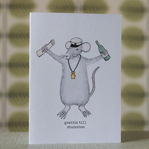 May include: A greeting card featuring a cartoon mouse wearing a graduation cap and a necklace with a teddy bear pendant. The mouse holds a scroll and a green bottle. The text "grattis till studenten" is at the bottom.