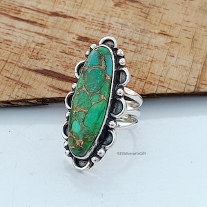 May include: A silver ring with a green and gold oval turquoise stone set in a decorative silver bezel. The ring has a wide band with a textured design.