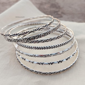 Puede incluir: Un conjunto de seis pulseras de plata con intrincados diseños florales y geométricos. Las pulseras están apiladas una encima de la otra, creando un aspecto en capas.