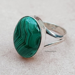 May include: A silver ring with a green malachite oval gemstone. The ring has a split band design. 925SilverartsGift
