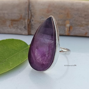 Könnte beinhalten: Ein Ring mit einem tropfenförmigen Amethyst-Edelstein, der in Sterlingsilber gefasst ist. Der Ring hat einen tiefvioletten Amethyst-Stein mit einer glatten, polierten Oberfläche.