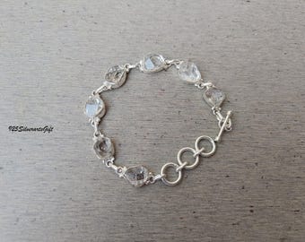 May include: A silver bracelet featuring clear, irregularly shaped gemstones. The bracelet has a toggle clasp and is displayed on a wooden surface. The text "925SilverartsGift" is visible in the lower left corner.