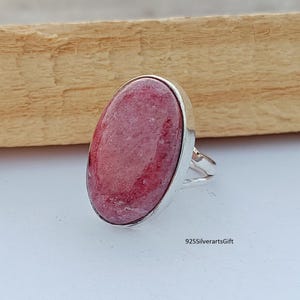 Könnte beinhalten: Ein silberner Ring mit einem großen ovalen rosafarbenen Edelstein. Der Ring ist in einer schlichten Silberfassung gefasst.