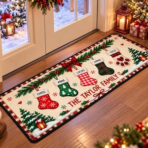 May include: A rectangular floor mat with a cream background featuring a festive Christmas theme. It displays five hanging stockings labeled Chris, Anna, Lucas, Emma, and Coco, with the text THE TAYLOR FAMILY printed in red. Green pine branches, red berries, and small Christmas trees decorate the mat.